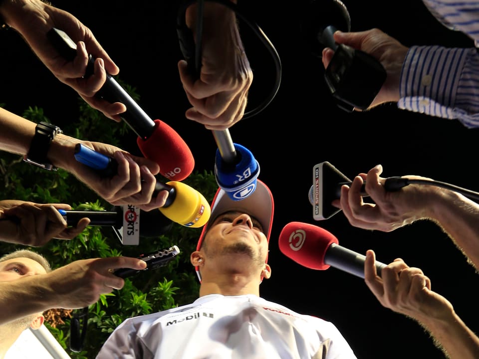 Journalisten strecken Lewis Hamilton unzähliche Mikrophone entgegen.
