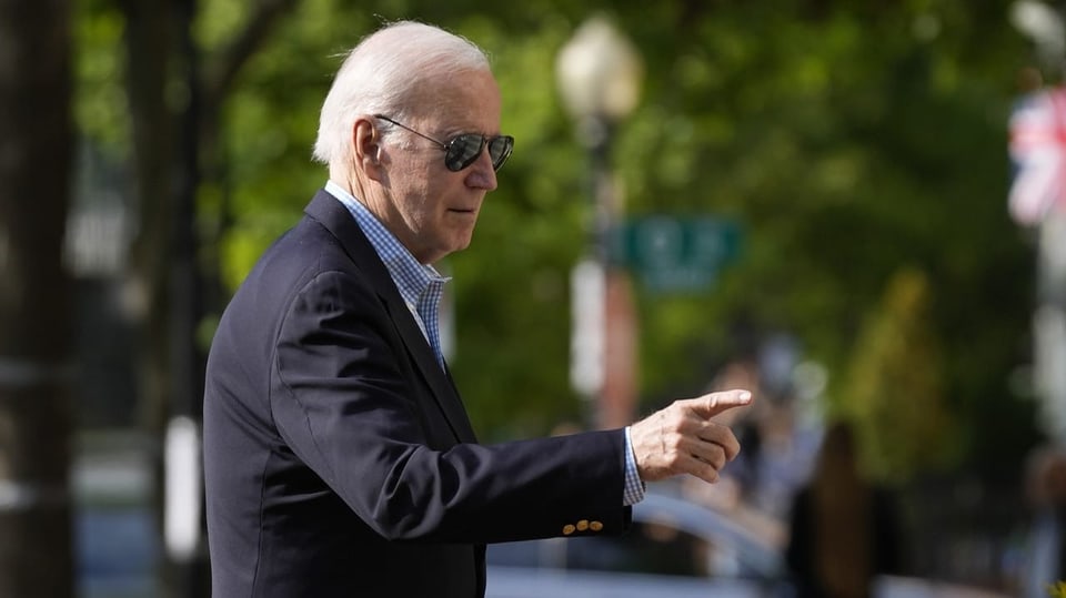 US President Joe Biden, wearing sunglasses and a suit, holds up his right index finger.