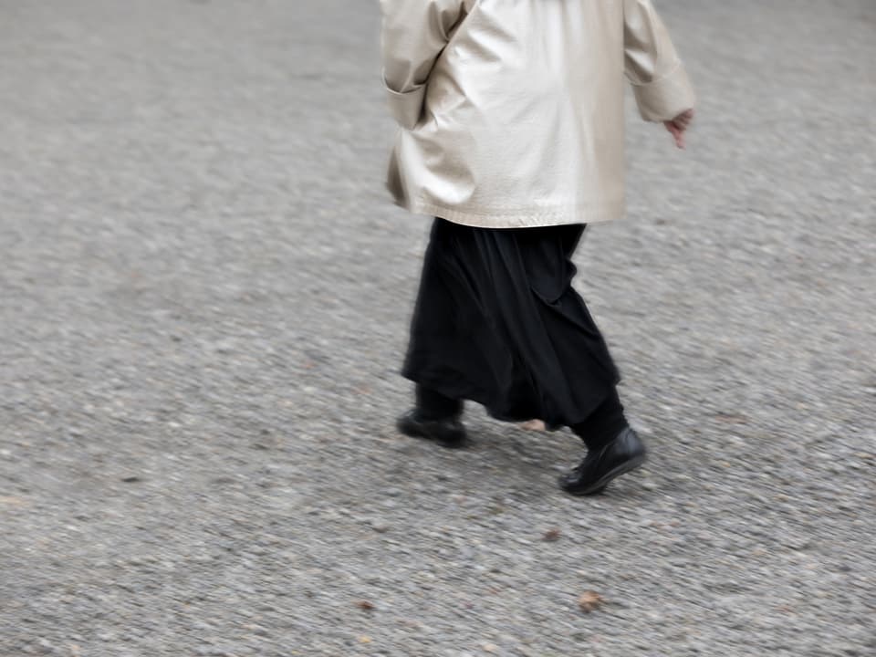 Eine Frau in schwarzem Rock geht über einen Platz.