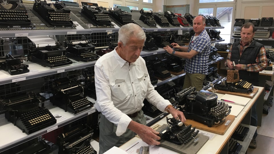  Drei Männer inmitten von Regalen voller Schreibmaschinen.