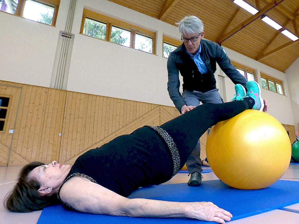Frau liegt am Boden, die Füsse auf einem Gymnastikball, und streckt ihren Körper durch.