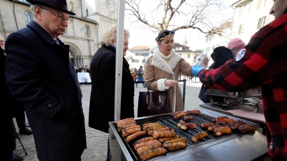 Menschen kaufen Wurst vom Grill am Platz vorm Grossmünster in Zürich.