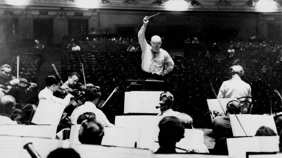 ein schwarz-weiss Foto eines Orchesters und eines Komponisten