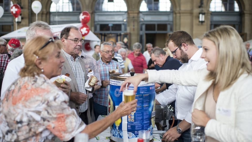 Viele Menschen trinken Bier und essen Sandwich. Man sieht ein Bierfass und eine Frau, die ein volles Bierglas bekommt.. 