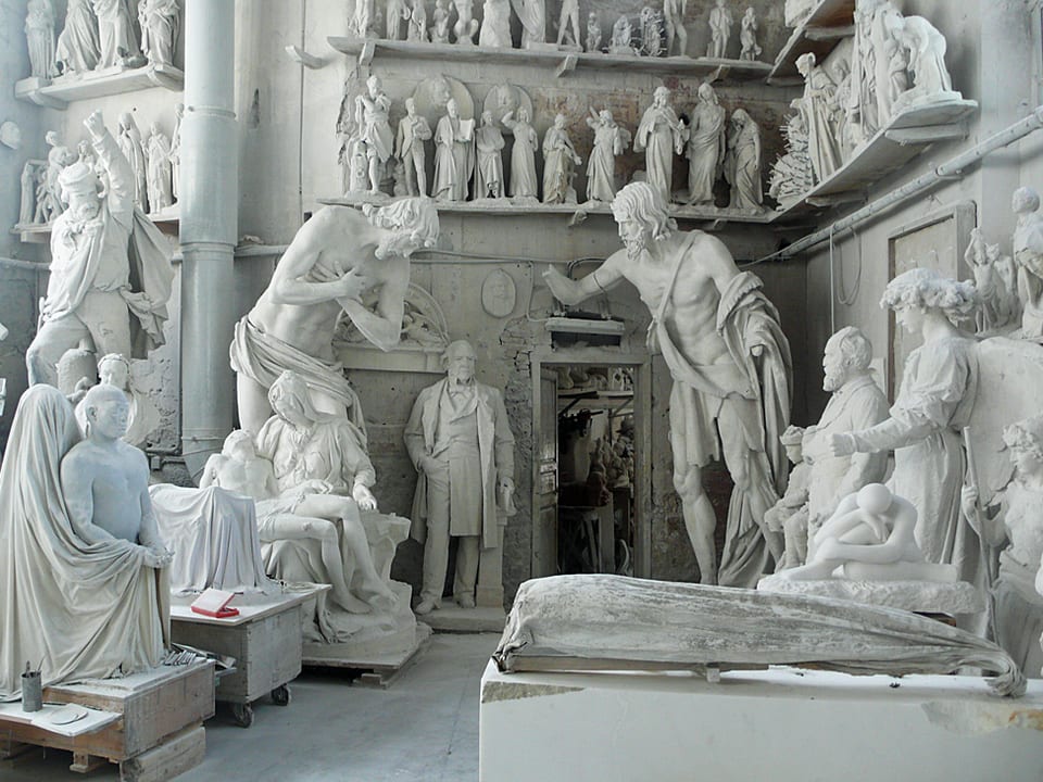 Aus Marmor gemeisselte Figuren stehen aufgereiht in einer Werkstatt.
