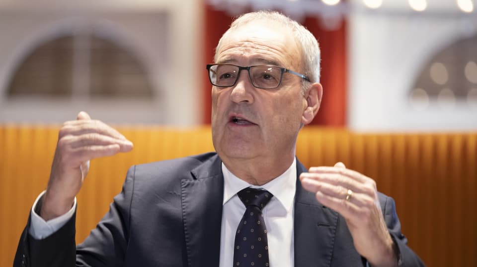 Guy Parmelin, bespectacled, graying hair, gesticulating in a suit, wedding ring.