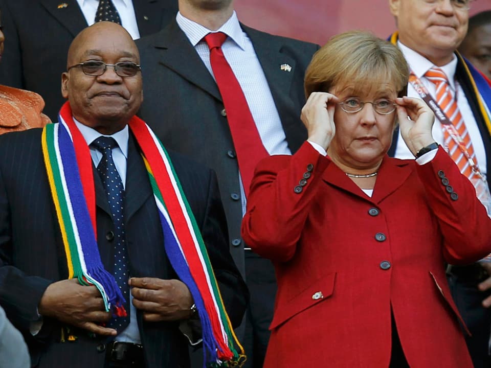 Zuma neben Merkel auf einer Tribüne. 
