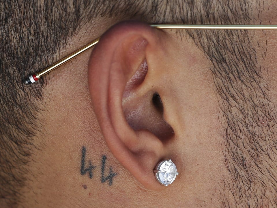 Der Ausschnitt von Lewis Hamiltons Ohr, das mit je einem Tattoo, Piercing und Brillant geschmückt ist.