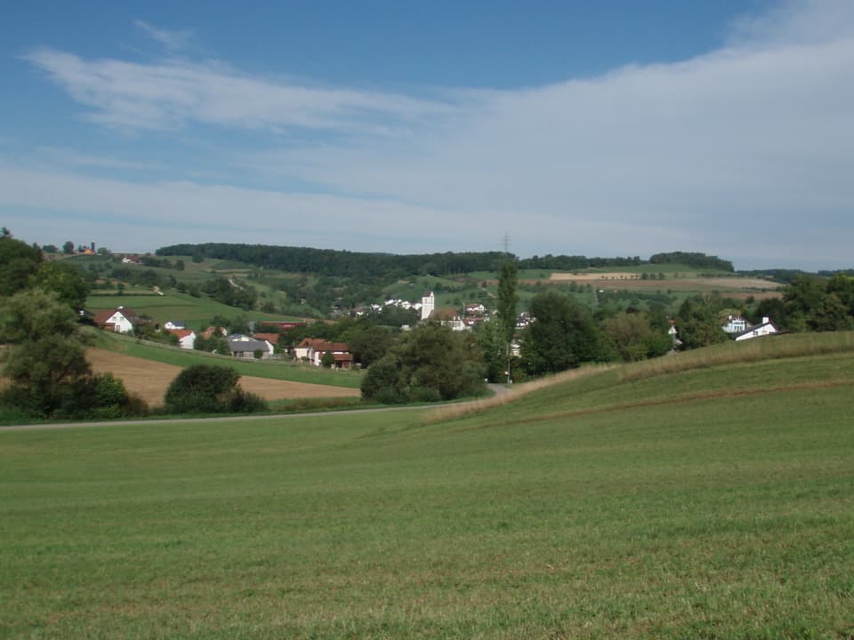 Blick auf das Dorf, im Vordergrund ist ein Acker zu sehen.
