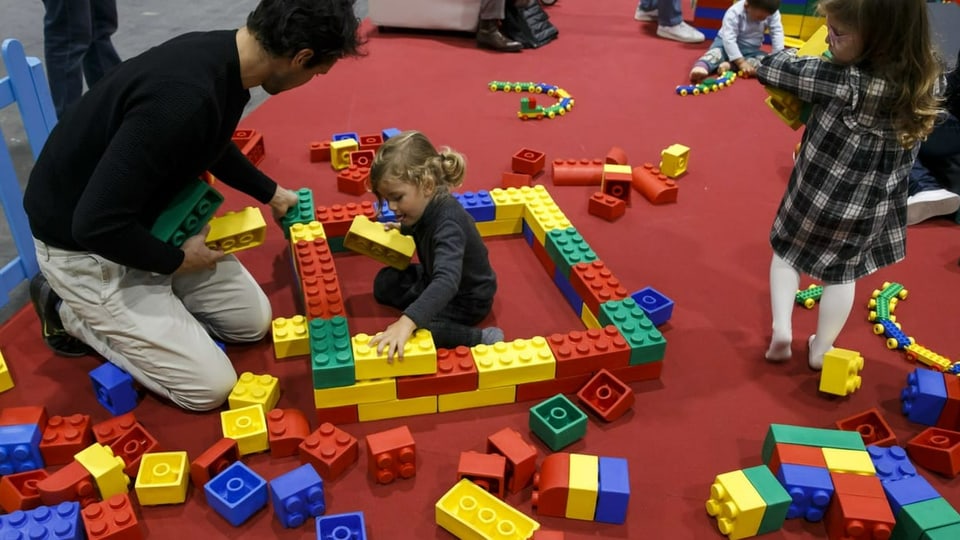 Kinder und Eltern spielen mit Legosteinen.