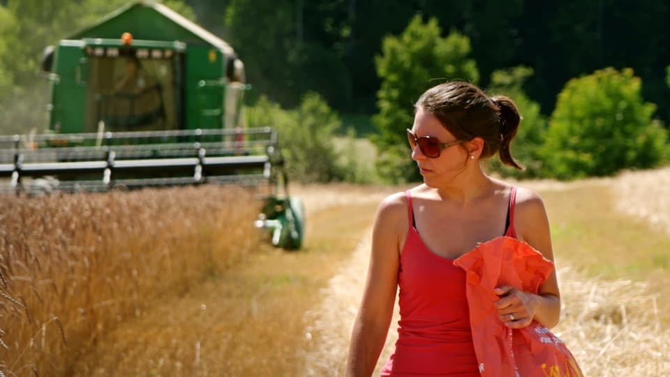 Claudia Zimmermann läuft durchs Getreidefeld. Hinter ihr fährt ein Mähdrescher.