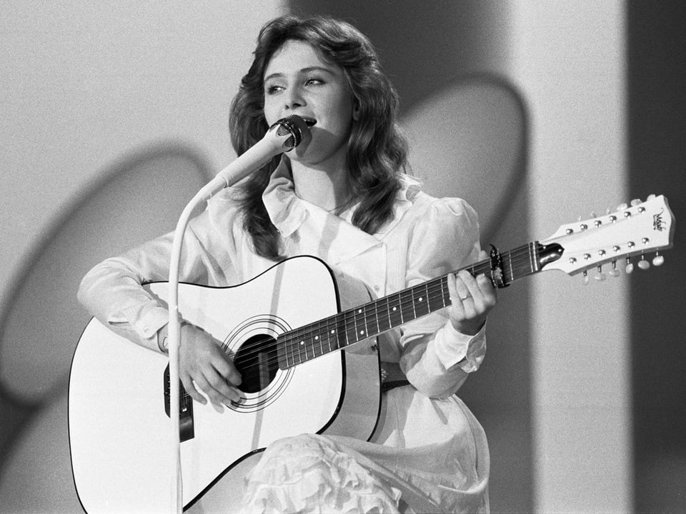 Eine junge Sängerin im weissen Kleid und mit einer weissen Gitarre.