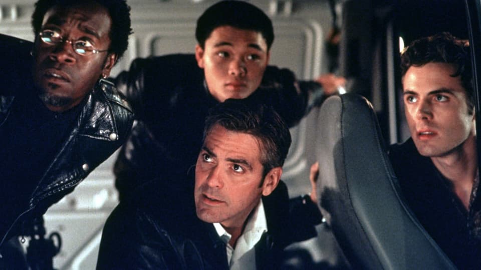 Szene aus dem Film "Ocean's Eleven": Im Inneren eines Kleinbusses, George Clooney sitzt in der Mitte, um ihn herum sind drei Männer. Alle sind in Schwarz gekleidet und schauen etwas verwirrt nach links vorne.
