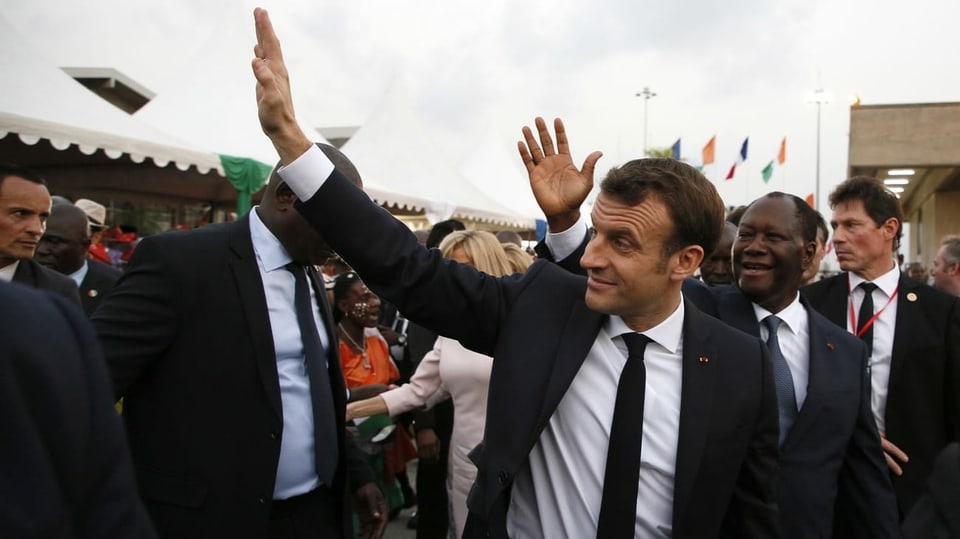 Macron winkt in Elfenbeinküste den Leuten zu. 