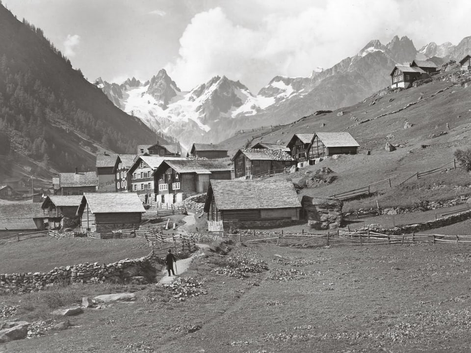 Altes Foto mit ungefähr 20 Bauernhäuser an einem Wanderweg.