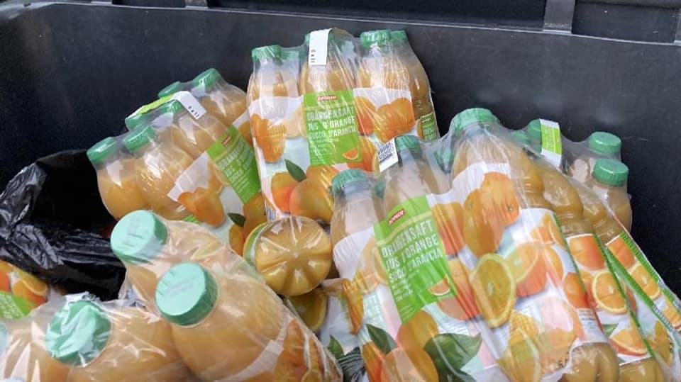 Viele Sechserpacks mit Orangensaft in einem Container entsorgt.