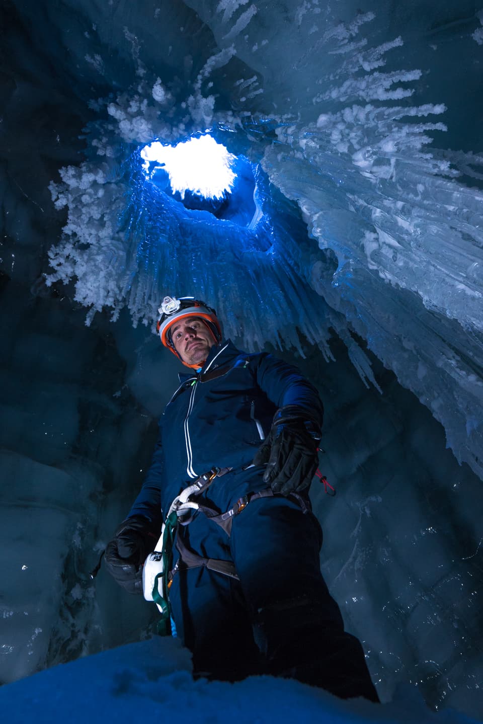 Ein Mann steht mit Stirnlampe in einem Gletscher