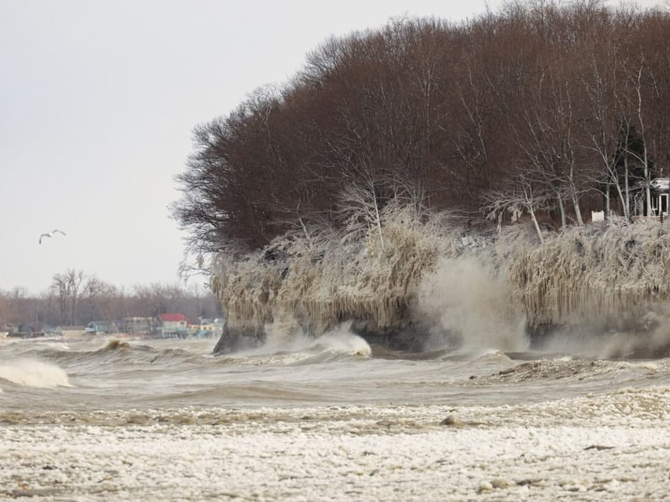 Bildaufnahme der Küste: Wellen krachen an die Küste. Es entsteht Gisch. Diese gefriert auf der Küstenoberfläche zu Eis.