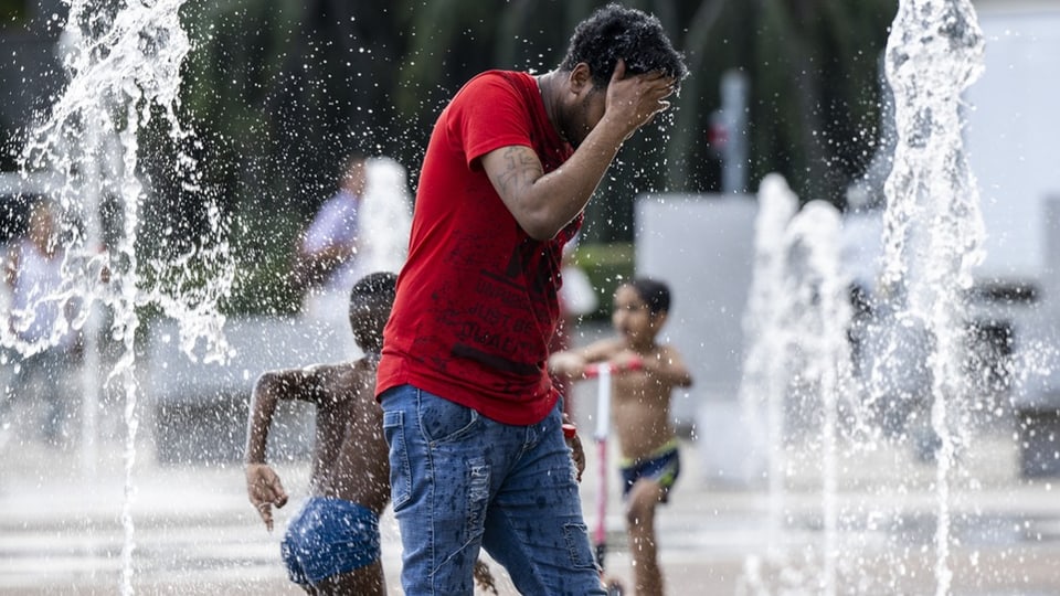 Ein Mann und Kinder netzen sich in einem Springbrunnen.