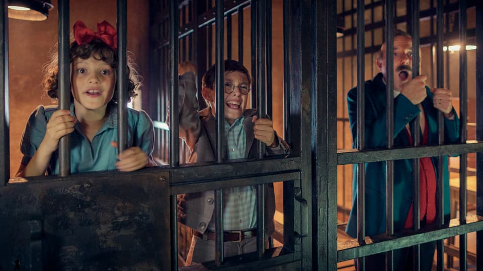 Im Gefängnis: In der linken Zelle sind ein Mädchen und ein junge eingesperrt, in der rechten ein Mann. Sie halten sich an den Gitterstäben fest und schreien.