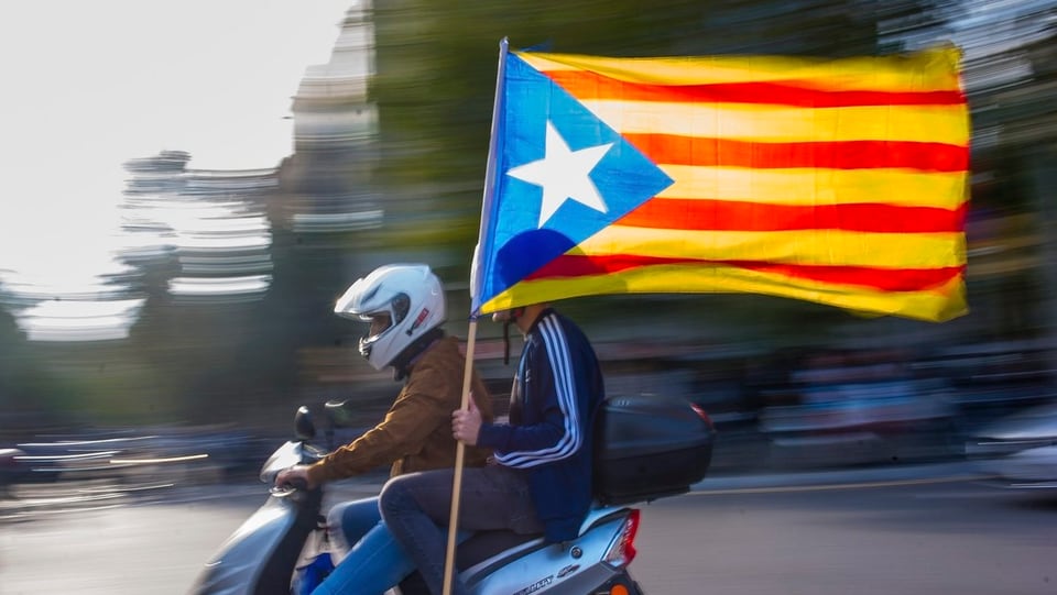 Zwei Personen auf Motorroller sitzend. Inoffizielle Flagge der katalanischen Unabhängigkeitsbewegung erkennbar