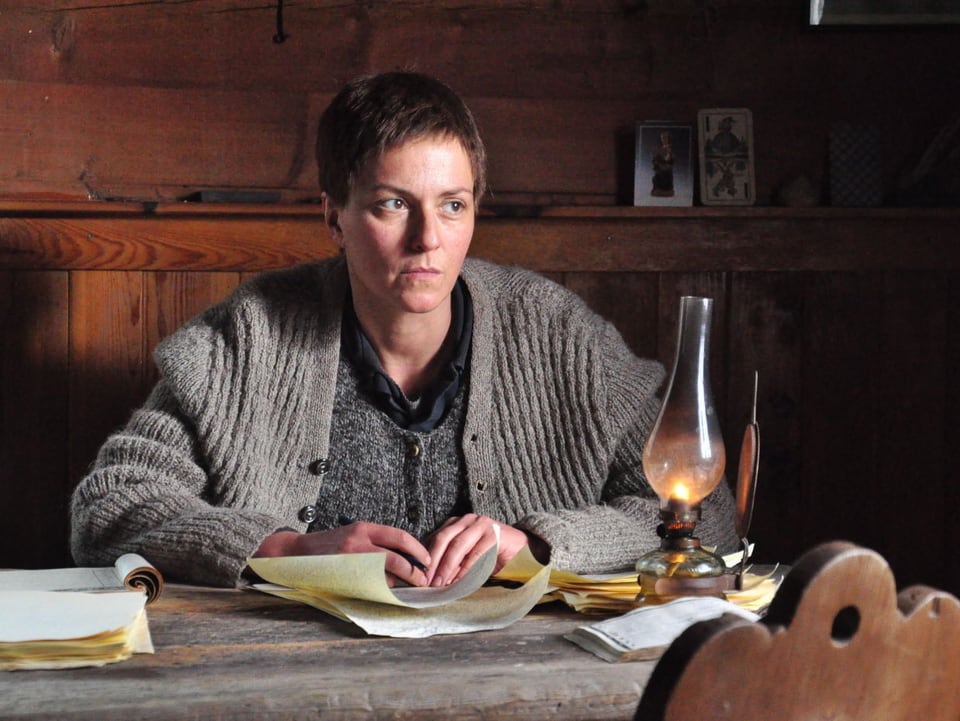 Schauspielerin Martina Gedeck sitzt in dieser Filmszene an einem Schreibtisch mit einer Öllampe.