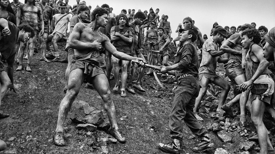 Schwarz-Weiss-Foto von zwei streitenden Arbeitern am Hang vor einer brasilianischen Goldmine.