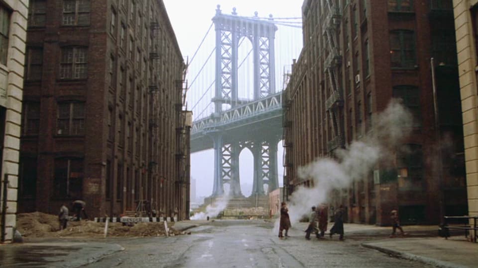 Mehere Personen gehen durch eine Strasse in new York. Im Hintergund ist eine riesige Brücke zu sehen. Bildausschnitt aus «Once Upon a Time in America».