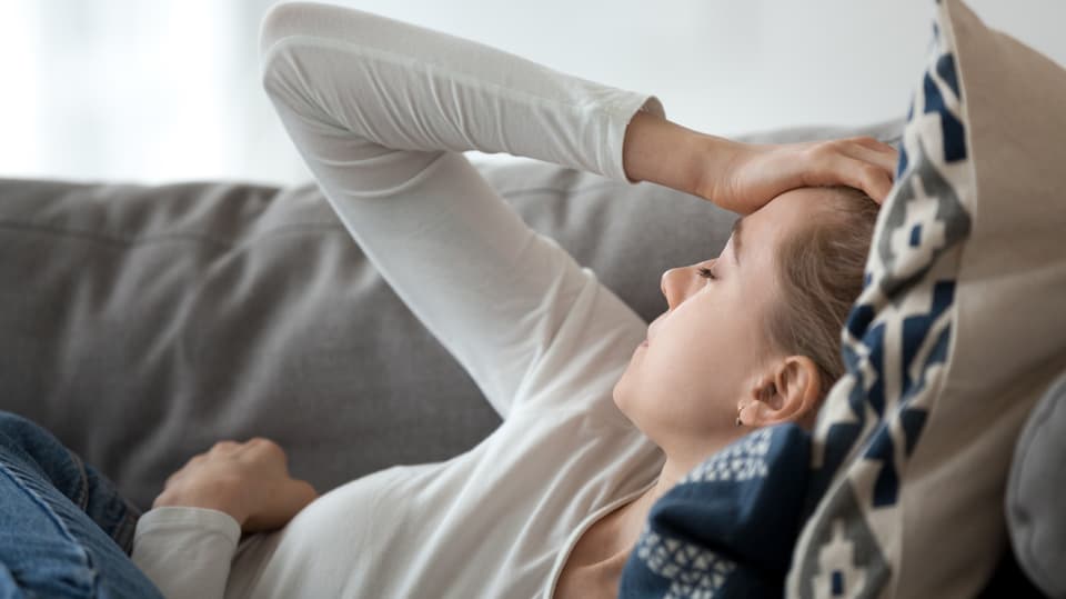 Frau liegt erschöpft auf Sofa und legt die Hand auf den Kopf