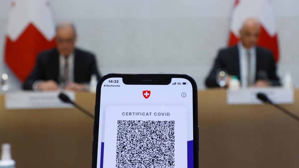 Im Hintergrund zwei Bundesräte, im Vordergrund ein Smartphonem mit einem Covid-Zertifikat