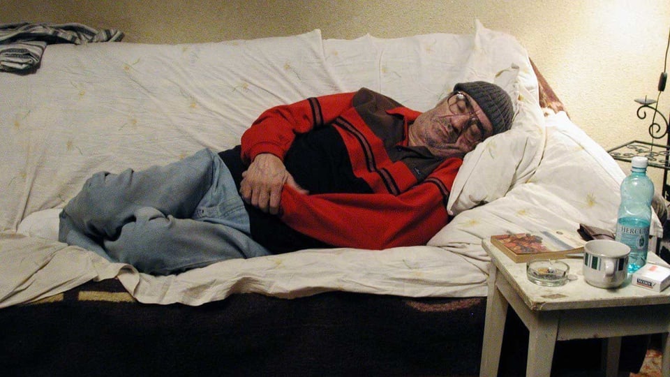Ein alter, kranker Mann leigt auf einem Sofa in einer schäbigen Wohnung.