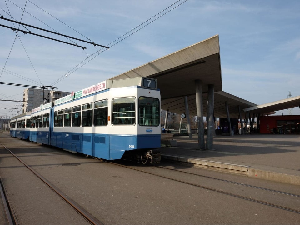 Ein blau-weisses Tram steht an der Endstation unter einem eckig geformten Betondach.
