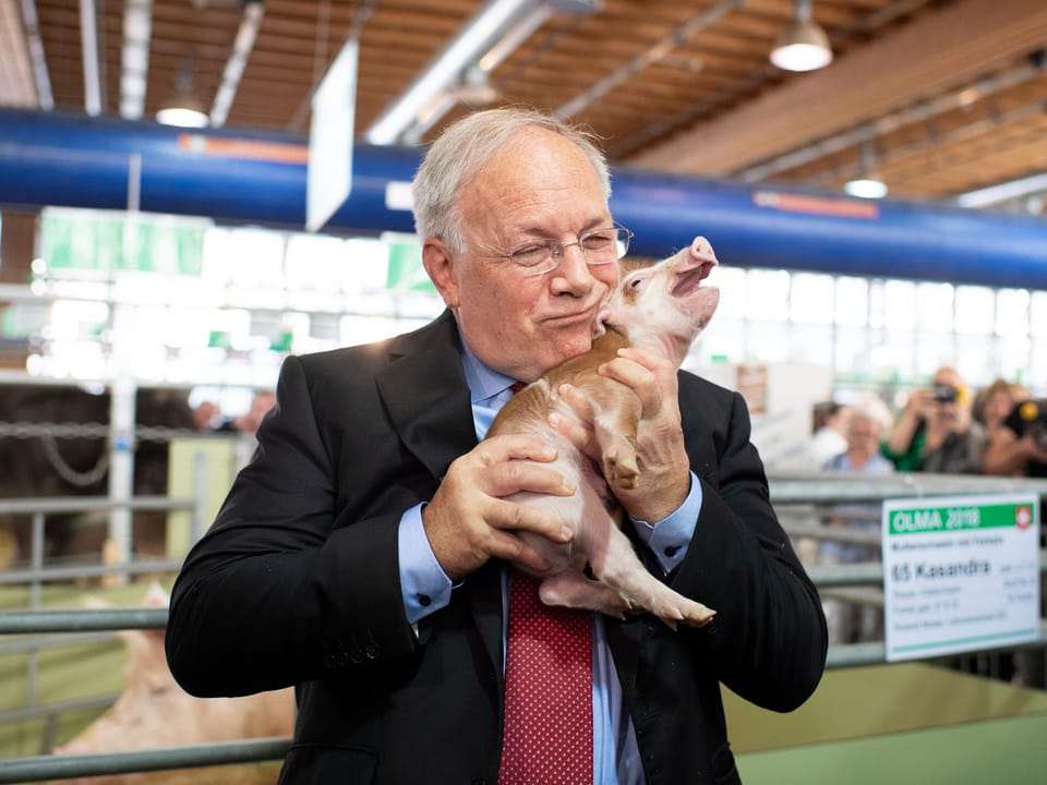 Schneider-Ammann mit einem Schweinchen im Arm.