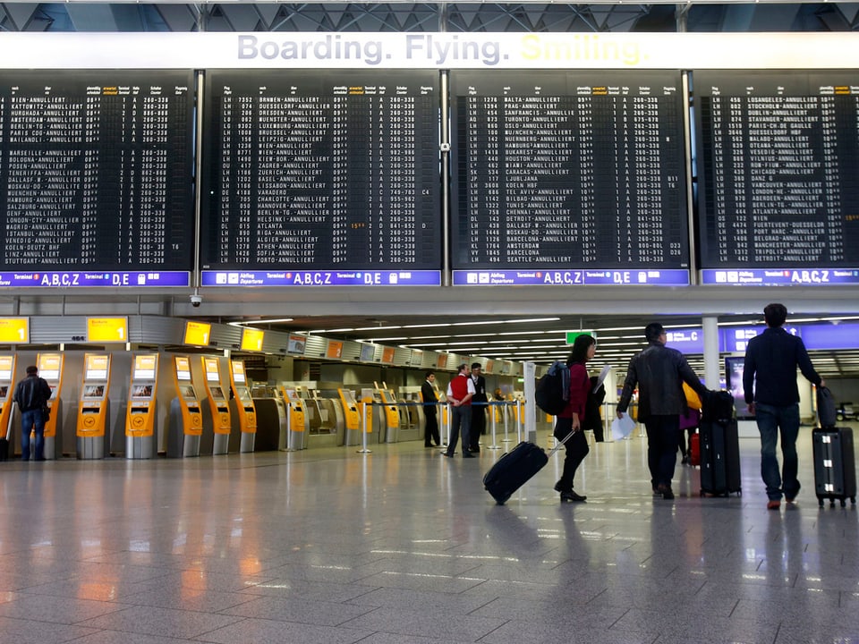 Drei einsame Passagiere vor der grossen Anzeigetafel am Flughafen Frankfurt