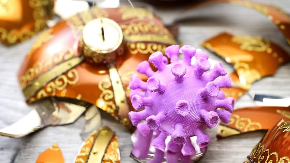Ein violetter Virus ist neben einer goldenen kaputten Weihnachtskugel zu sehen.