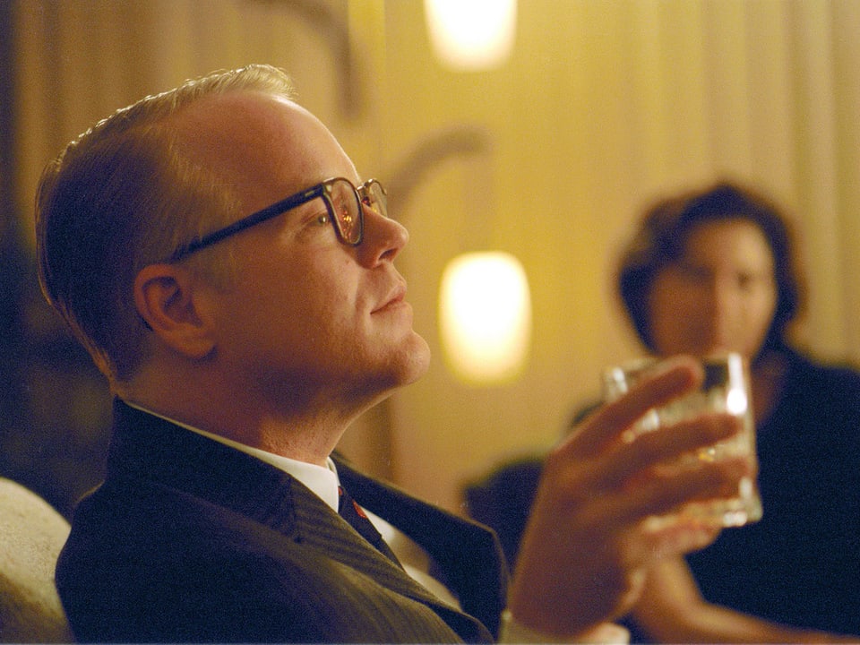 Hoffman als Capote sitzend mit einem Whiskey-Glas
