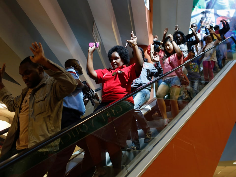 Besucher verlassen die Shopping-Mall mit erhobenen Händen.