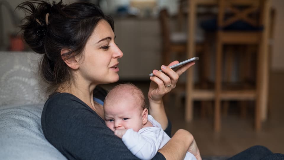 Frau hält Baby und spricht ins Handy