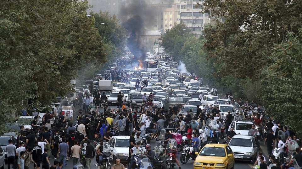 Proteste: Hunderte Menschen sind auf einer Strasse, die gefüllt ist mit querstehenden Autos. Dahinter ist Rauch zu sehen