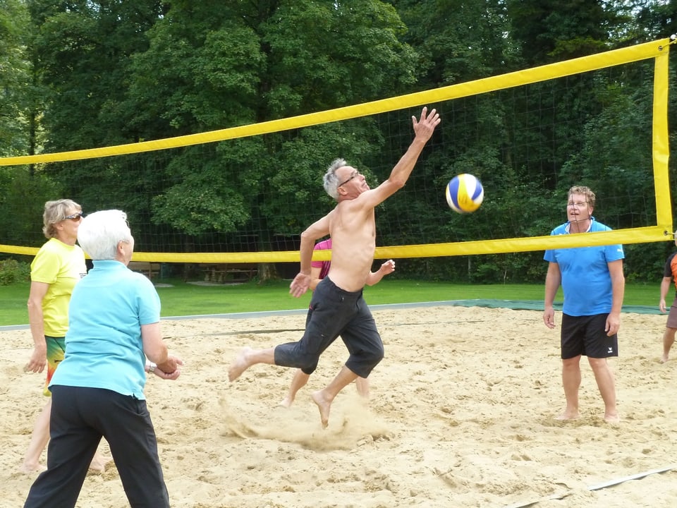 Durchtrainierter Senior wirft einen Volleyball übers Netz.