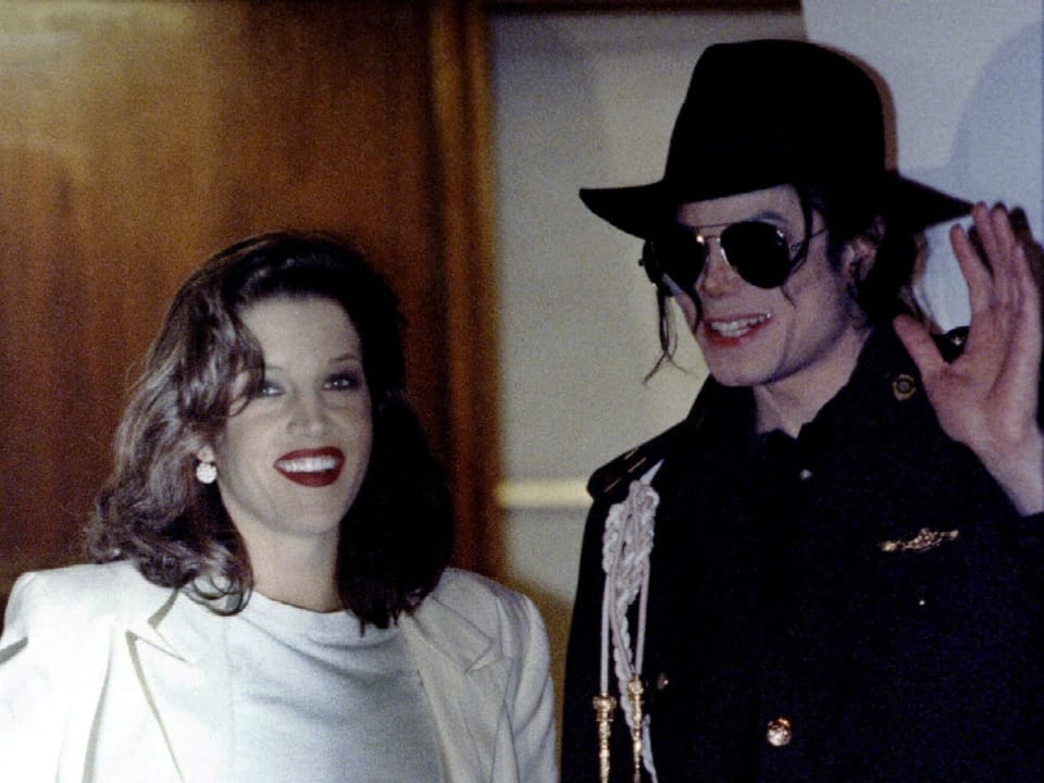 Lisa Marie Presley und Michael Jackson lächeln in die Kamera, Jackson winkt.
