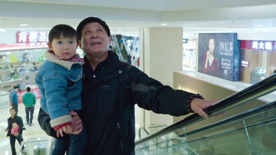 Foto chinesischer Mann mit Kind auf dem Arm auf der Rolltreppe