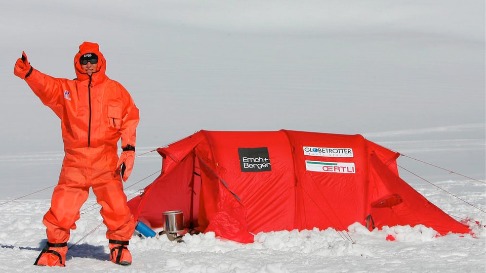 Thomas Ulrich auf einem Gletscher in rotem Genzkörperanzug, neben rotem Zelt.