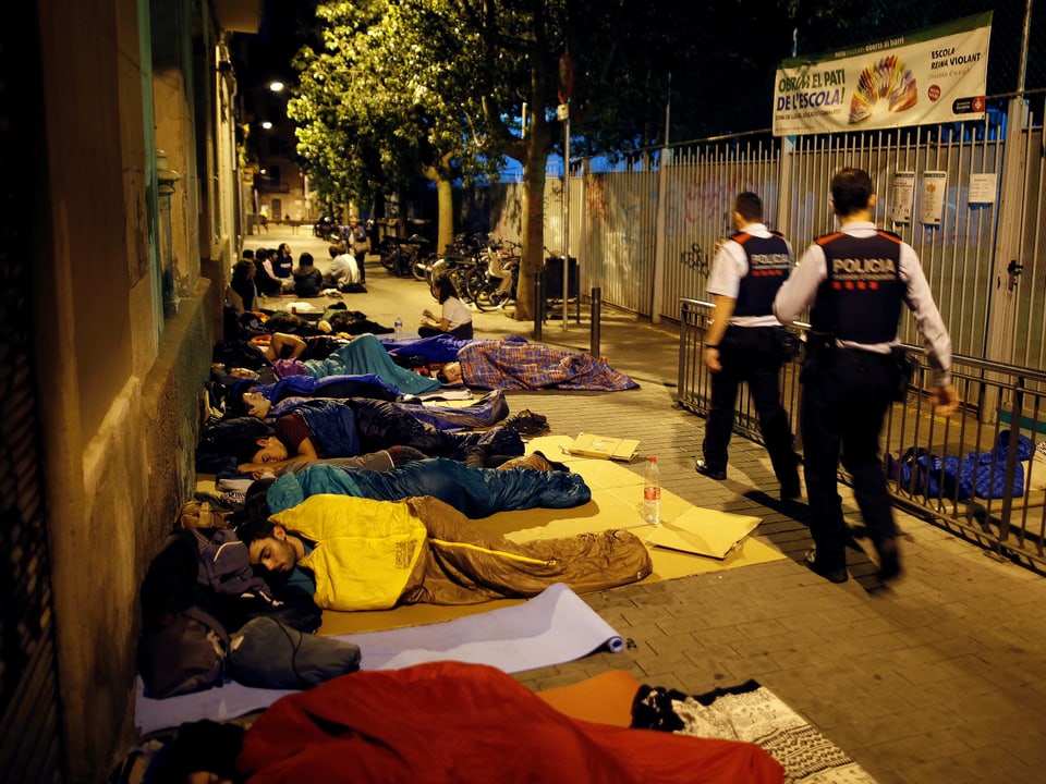 Zwei Polizisten gehen an Schlafenden in Schlafsäcken vorbei.