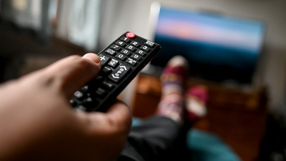 Eine Hand zeigt mit der Fernbedienung auf einen Fernseher.