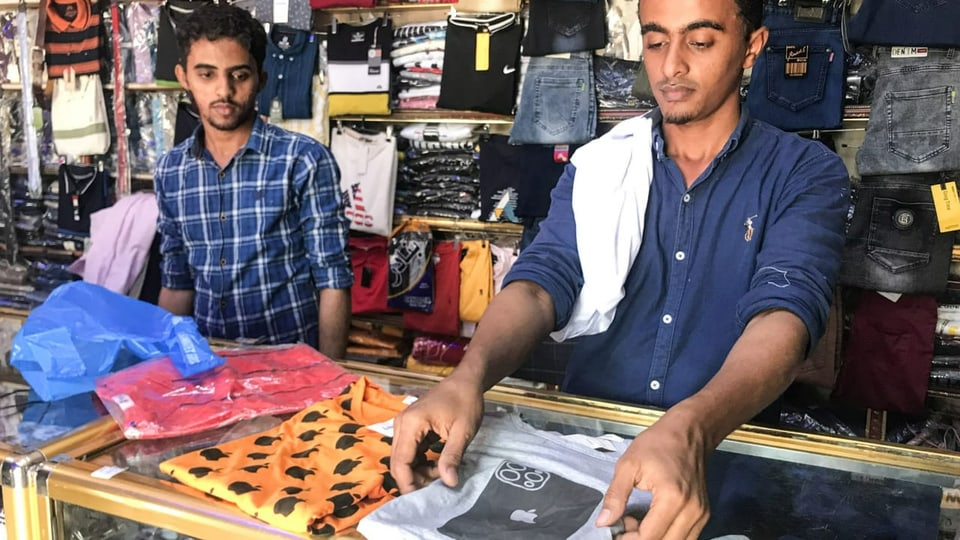 Ein Verkäufer präsentiert ein T-Shirt mit einem abgebildeten iPhone.