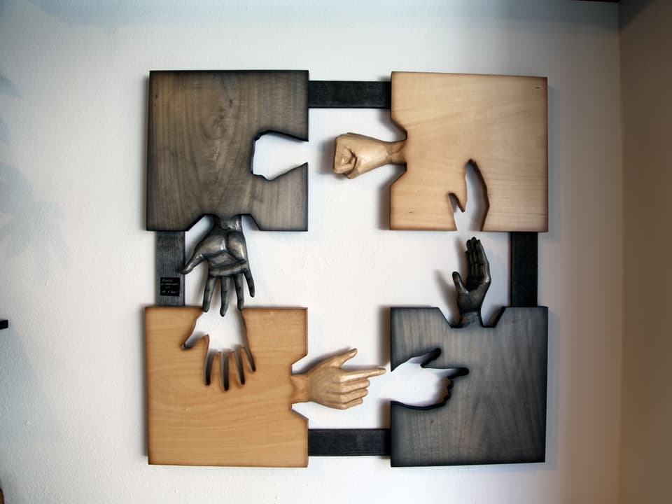 An der Wand in der Holzbildhauerei hängt ein Kunstwerk, welches aus vier Händen in verschiedenen Positionen besteht.
