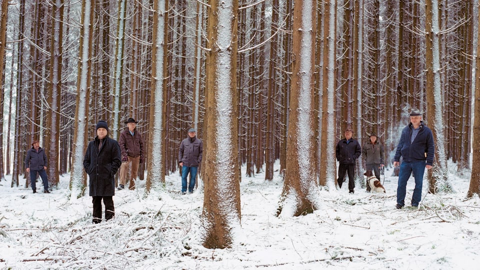 Männer stehen in einem verschneiten Wald.