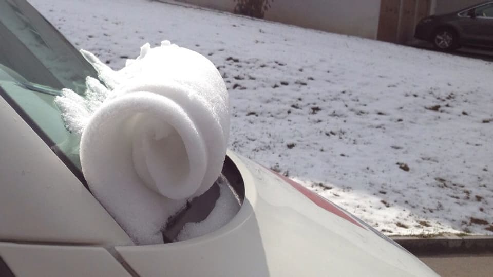 Eine dünne Schneeschicht auf einer Autofrontscheibe hat sich von oben nach unten aufgerollt.