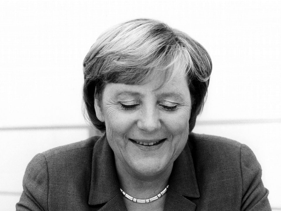 Ein Schwarz-weiss-Porträt von Angela Merkel, die lächelnd nach unten schaut. 